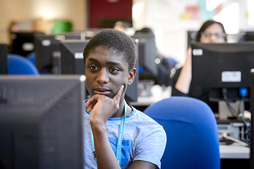 a young man with an expression of deep concentration sits at a workstation in a computing lab